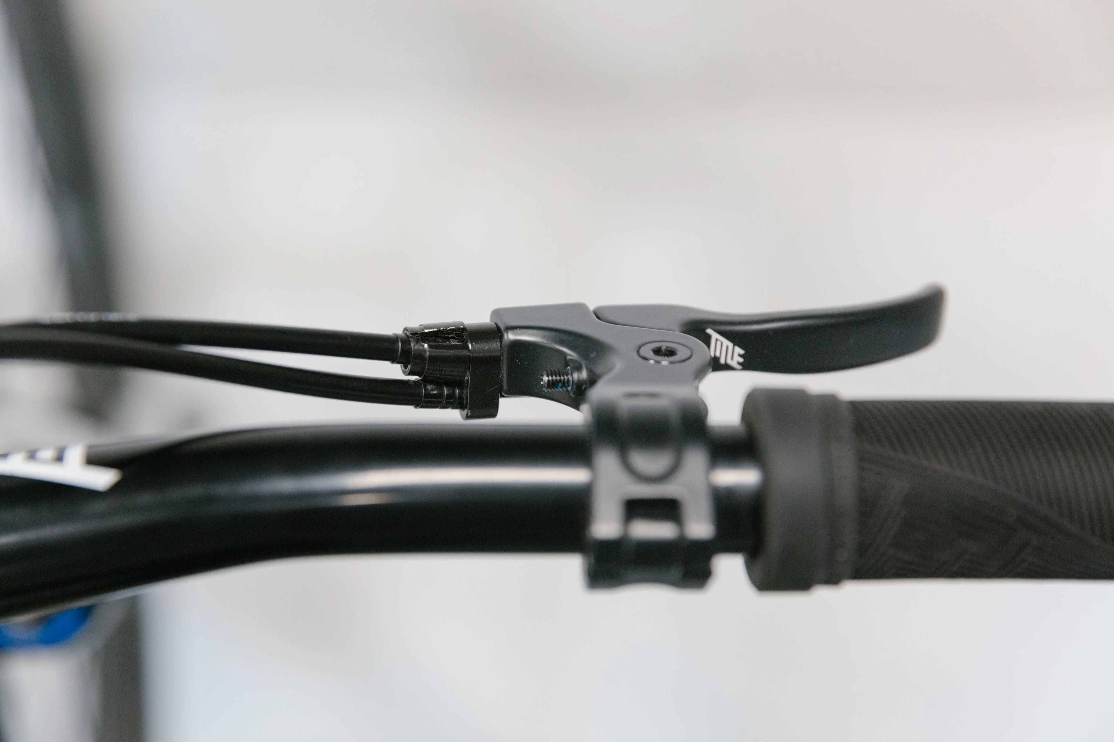 Close-up of a black TITLE G1 Gyro brake lever and system on a bicycle handlebar with a black grip and cables, against a white background