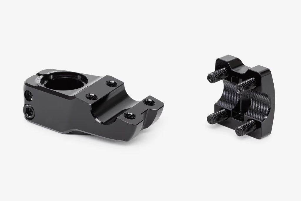Side view of black bicycle stem with removable clamp components separated, showing the main stem body and detachable handlebar clamp with visible hex bolts and threaded hardware