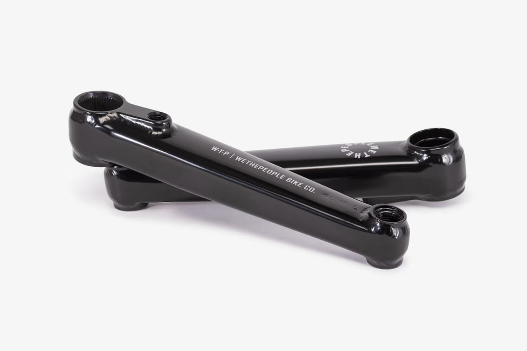 A pair of black WeThePeople Logic BMX cranks, showcasing their robust 3-piece design and durable square arms made from heat-treated 4130 chromoly. Includes a 22mm spindle and compatible with WTP Compact Mid bottom bracket.