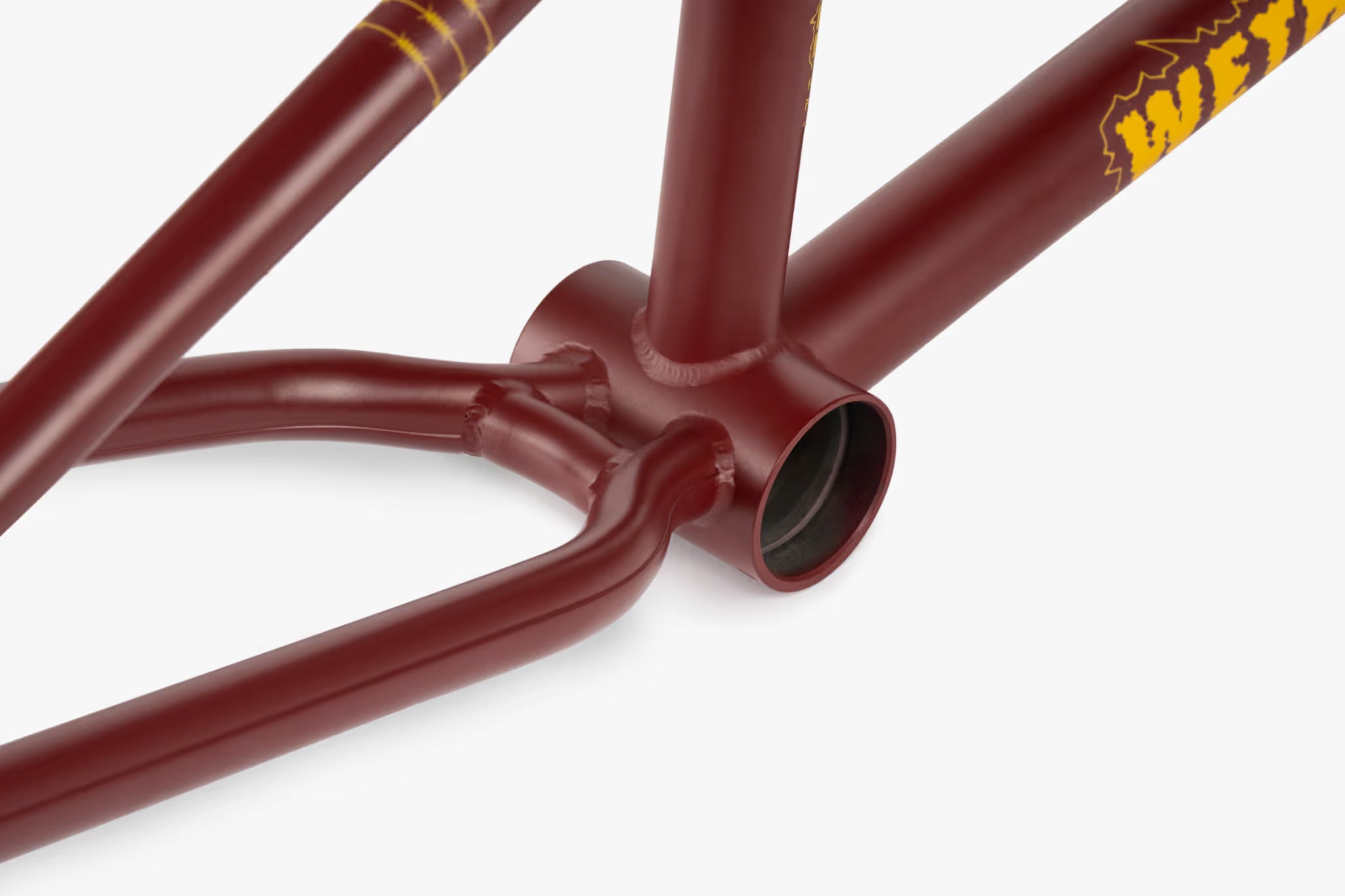 Close-up of a matte burgundy We The People Pathfinder BMX frame, highlighting the bottom bracket and the iconic yellow We The People logo on the downtube