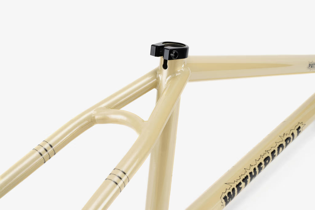 Close-up of a cream-colored We The People Pathfinder BMX frame, showcasing the integrated seat clamp, head tube details, and 'WETHEPEOPLE' branding along the chainstay