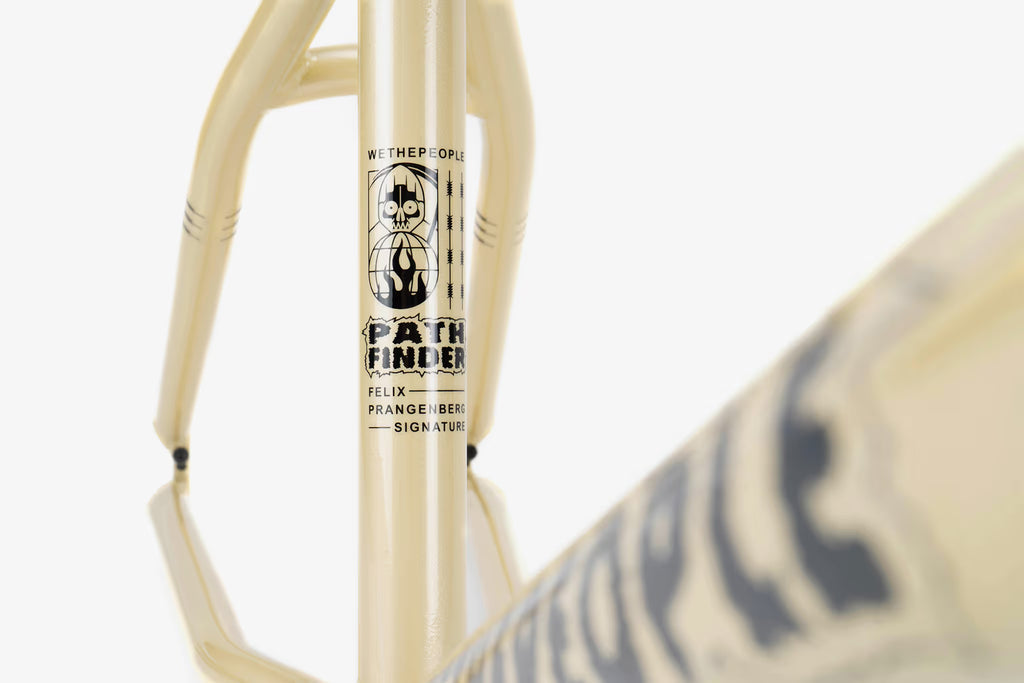 Close-up of a cream-colored We The People Pathfinder BMX frame, featuring the 'WETHEPEOPLE PATHFINDER FELIX PRANGENBERG SIGNATURE' branding in black text and a skull graphic on the downtube. The frame's clean lines and durable construction are highlighted.