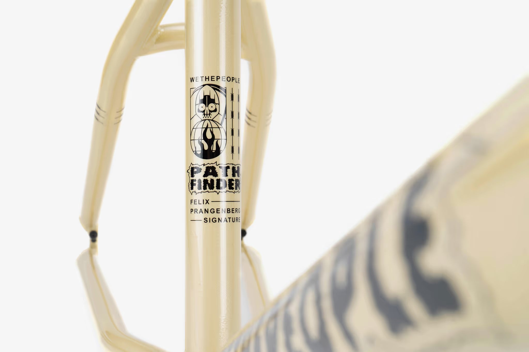 Close-up of a cream-colored We The People Pathfinder BMX frame, featuring the 'WETHEPEOPLE PATHFINDER FELIX PRANGENBERG SIGNATURE' branding in black text and a skull graphic on the downtube. The frame's clean lines and durable construction are highlighted.