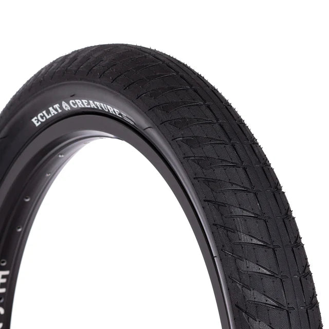 Close-up profile view of the Éclat Creature BMX Tire, all-black, highlighting the agressive tread blocks and CREATURE sidewall branding.
