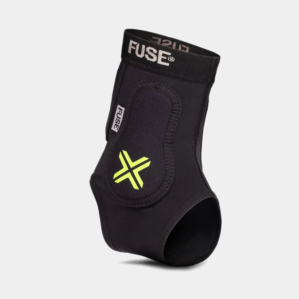 FUSE Omega Ankle Protector, black, angled view highlighting the yellow/neon 'X' logo on the protective padding and the elastic FUSE band.