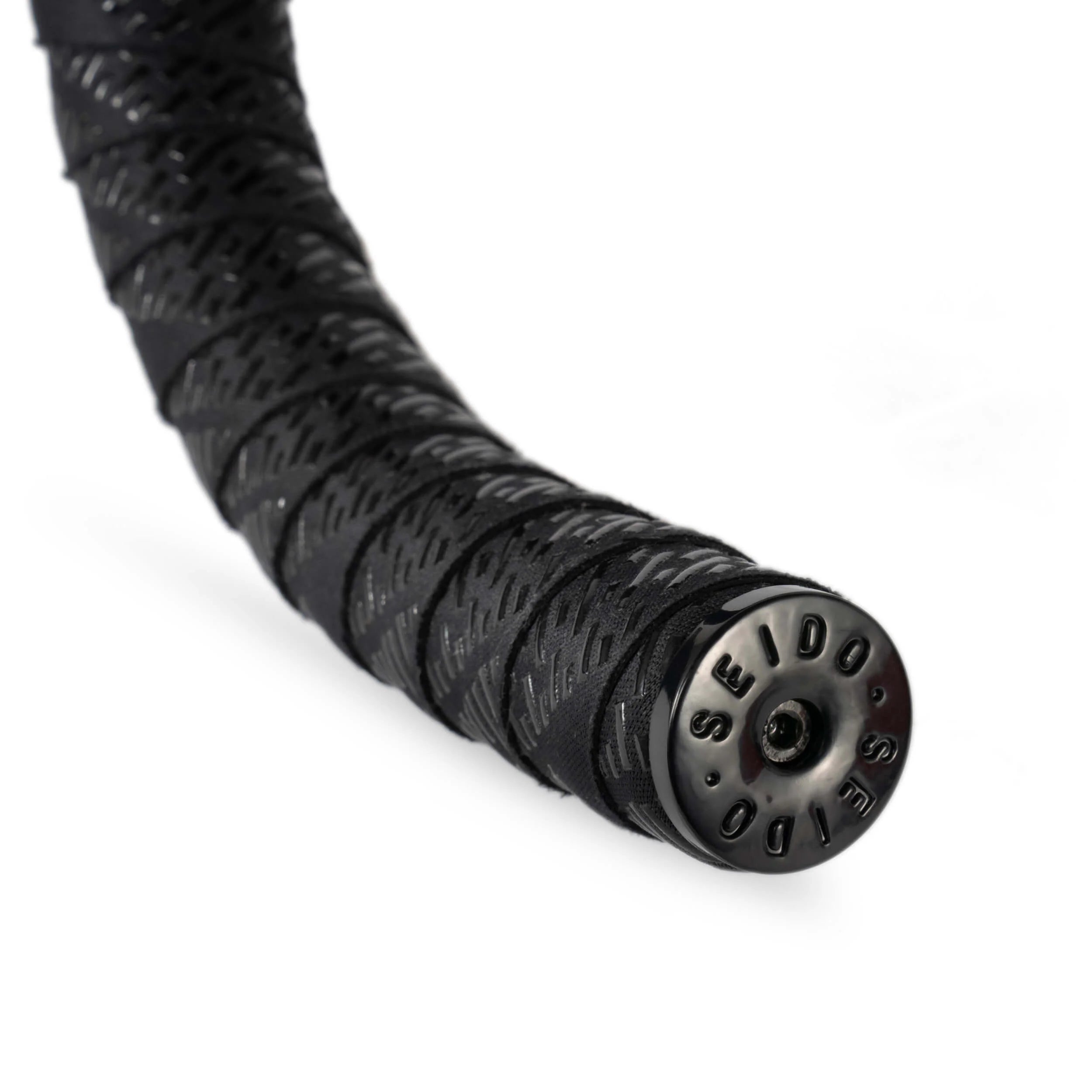 Close-up view of the SEIDO TAB Handlebar Tape, black, highlighting the textured pattern and the glossy black metal SEIDO bar end plug.